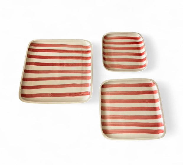 Set of four square ceramic plates with red and white stripes on a white background