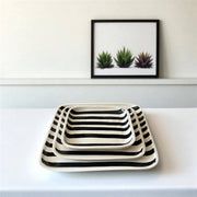 Set of three black and white striped trays on a white surface with a framed picture of plants in the background.