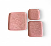 Set of three pink square plates with textured patterns on a white background