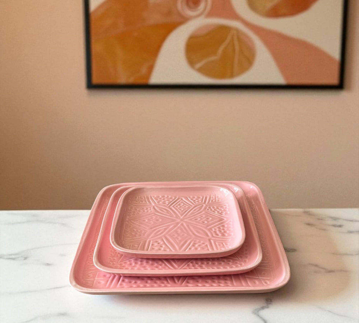 Set of pink textured trays on a marble surface with a abstract art piece in the background.