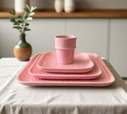 Set of pink ceramic dishes on a table with a plant and vase in the background