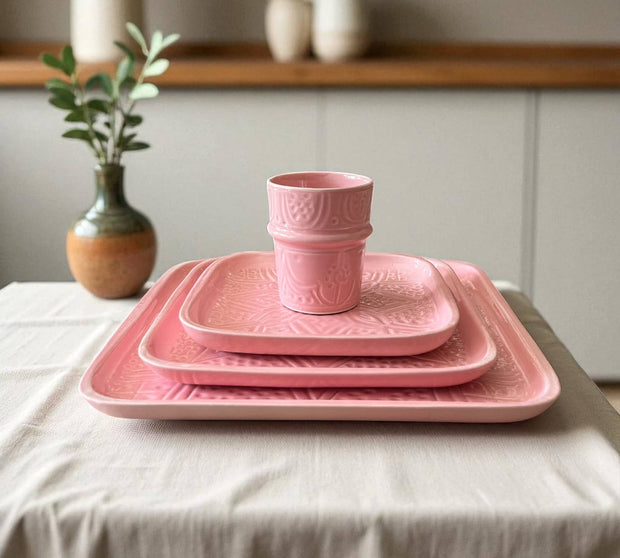 Set of pink ceramic dishes on a table with a plant and vase in the background