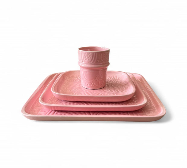 Set of pink ceramic dishes including a cup, plate, and bowl on a white background