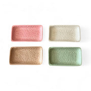 Four rectangular ceramic trays in pink, beige, and green on a white background