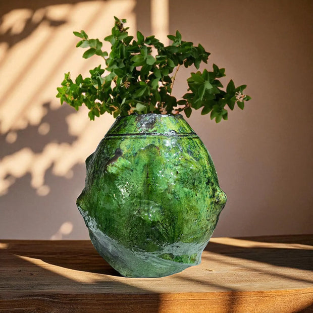 Green textured vase with plant on a wooden surface