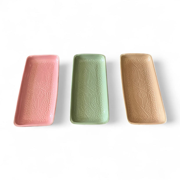 Three rectangular ceramic trays in pink, green, and beige on a white background
