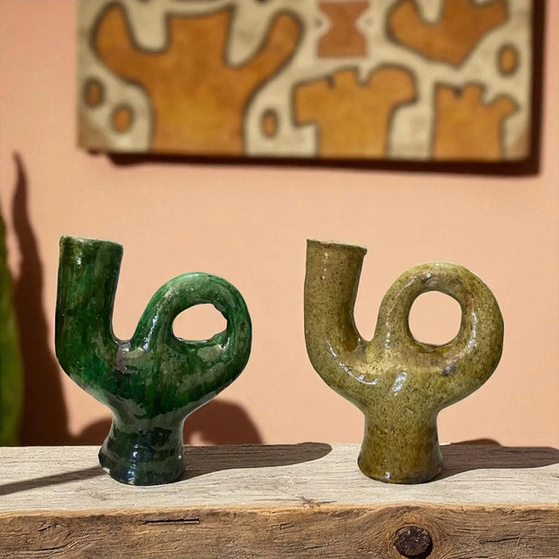 Two green & yellow ceramic  on a wooden surface with abstract art in the background.