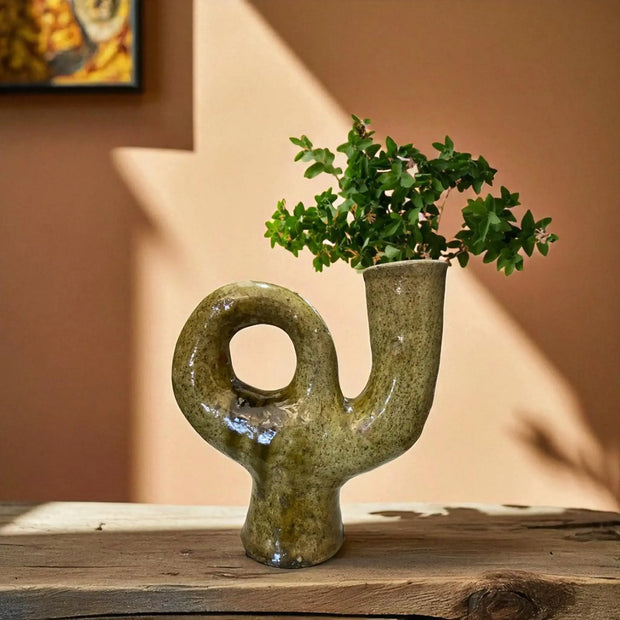 Decorative yellow vase with a unique shape on a wooden surface against a beige wall.