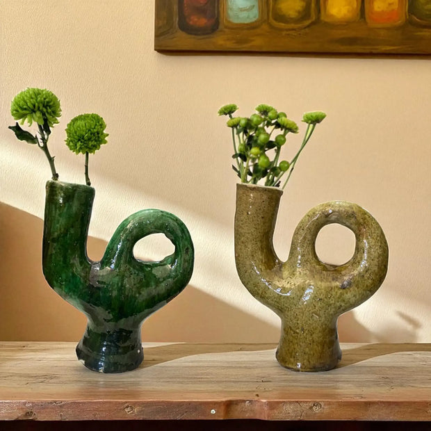 Two unique ceramic vases with abstract designs holding greenery on a wooden surface.