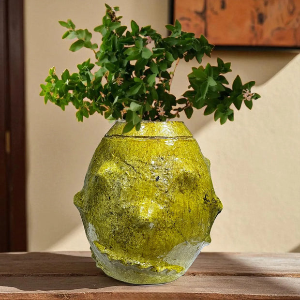 Yellow textured vase with plant on a wooden surface