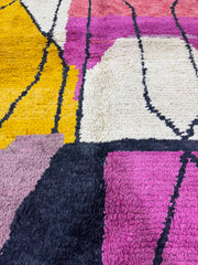 Close-up of a textured rug with geometric patterns in purple, yellow, and white.