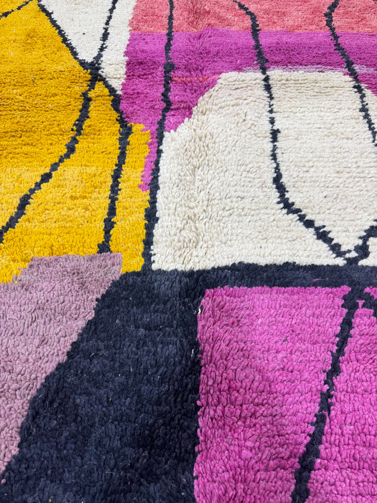 Close-up of a textured rug with geometric patterns in purple, yellow, and white.