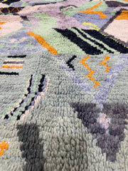Close-up of a textured rug with geometric patterns in gray, black, orange, and green.