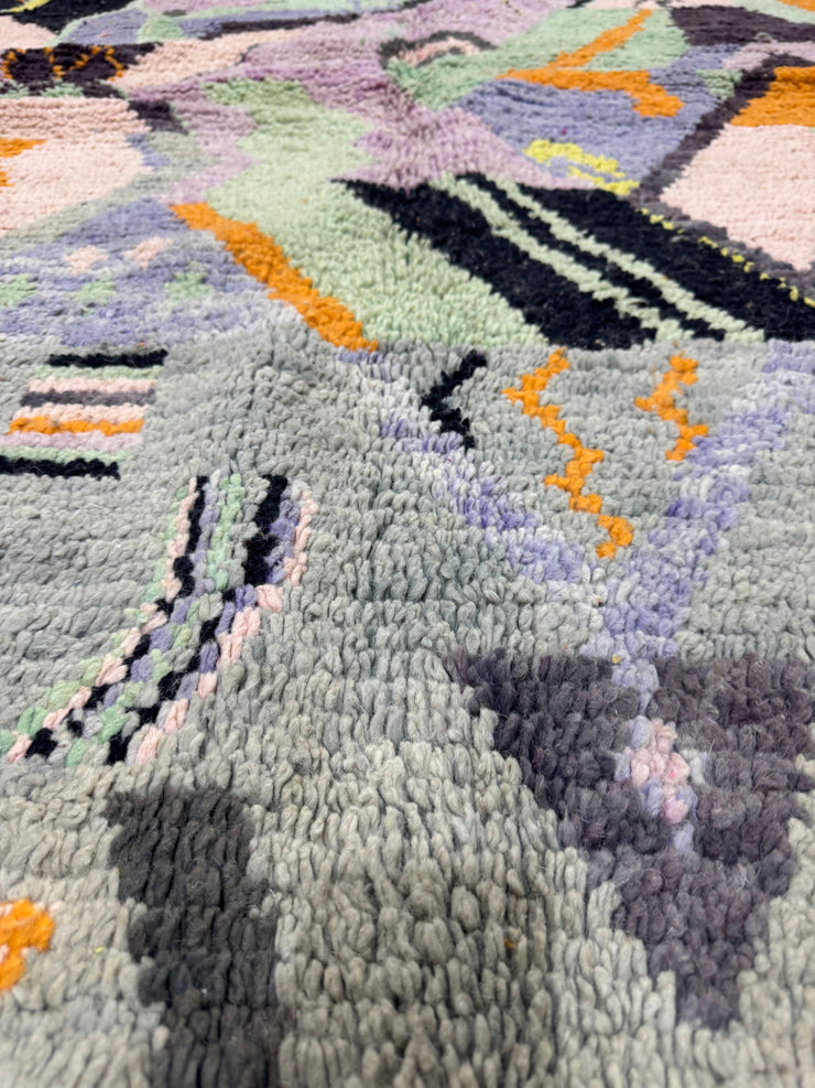 Close-up of a textured rug with geometric patterns in gray, black, orange, and green.