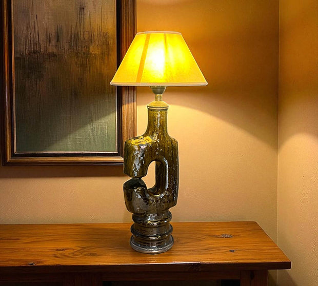 Decorative table lamp with a yellow shade on a wooden surface, with a painting in the background.