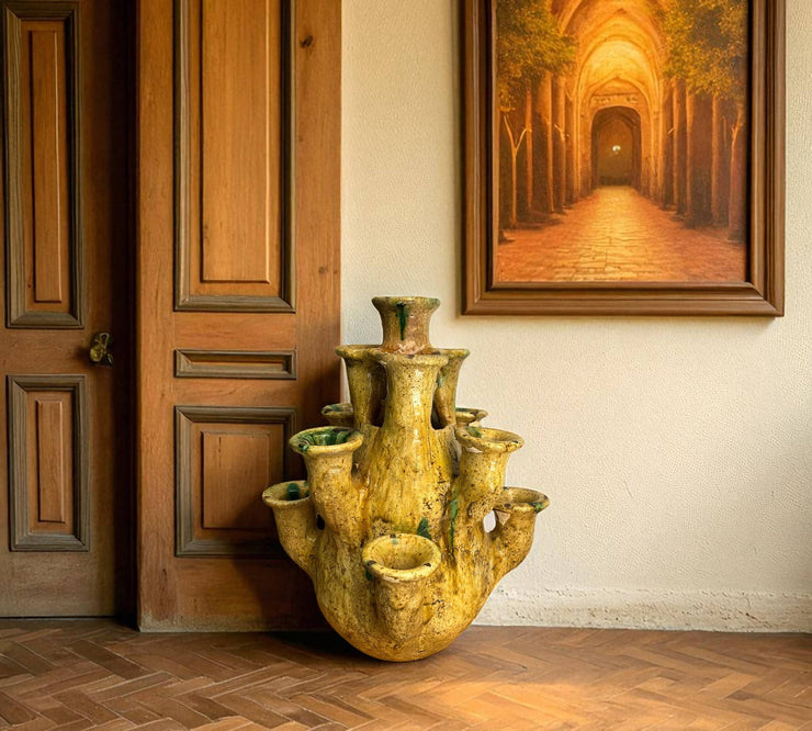 Decorative yellow vase on a wooden floor with a painting of a tunnel in the background.
