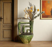 Decorative vase with dried flowers on a wooden floor next to a wooden door and wall art.