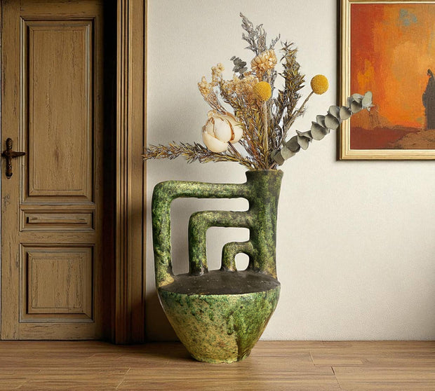 Decorative vase with dried flowers on a wooden floor next to a wooden door and wall art.