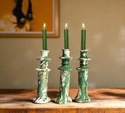 Three green candles in decorative candlesticks on a wooden surface with a blurred background
