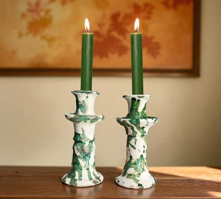 Two green candles in decorative candlesticks on a wooden surface with a blurred background