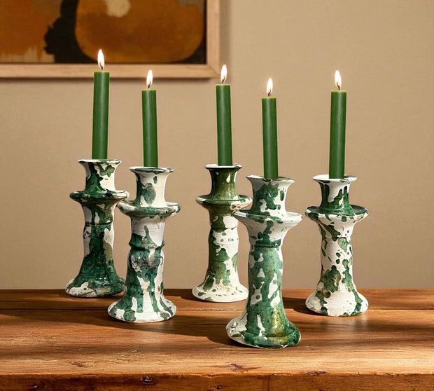 Set of five green candles in decorative candle holders on a wooden surface with a beige wall background.