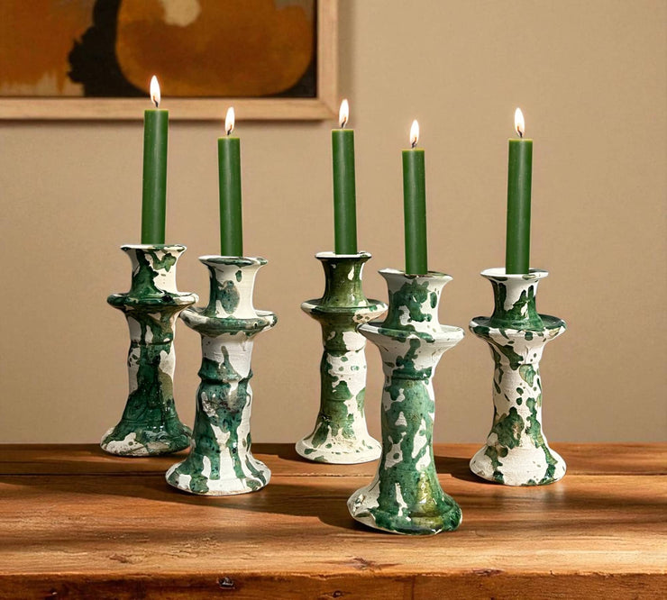 Set of five green candles in decorative candle holders on a wooden surface with a beige wall background.