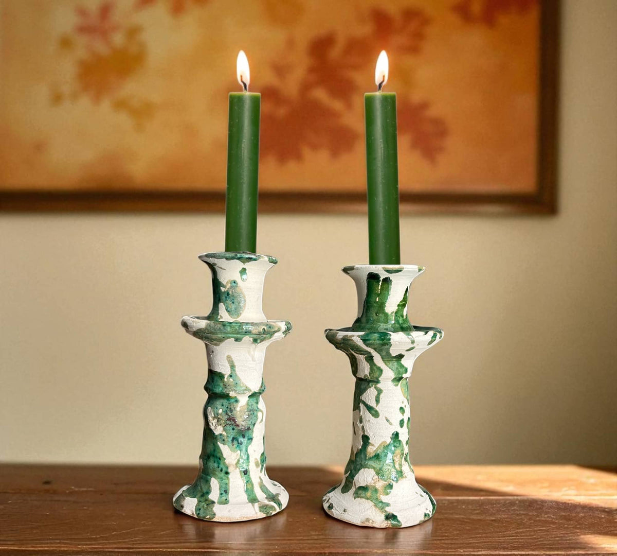 Two green candles in decorative candlesticks on a wooden surface with a blurred background