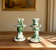 Two green and white ceramic candle holders on a wooden surface with a blurred background.