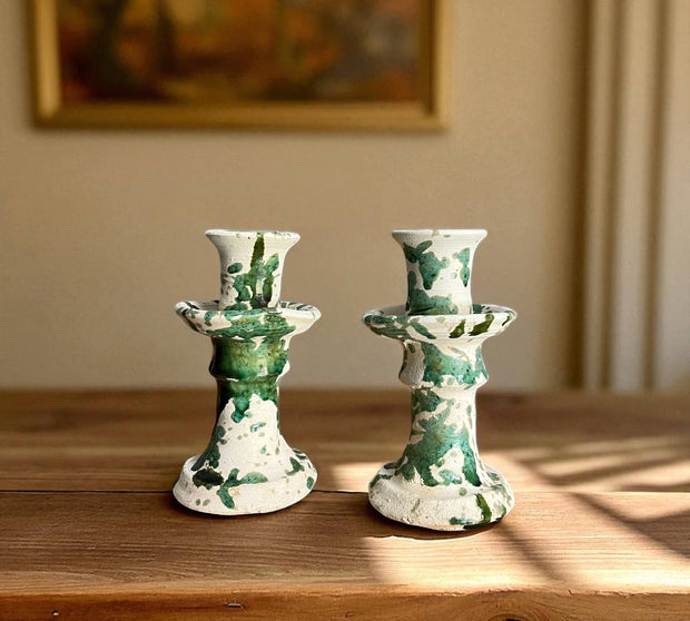 Two green and white ceramic candle holders on a wooden surface with a blurred background.