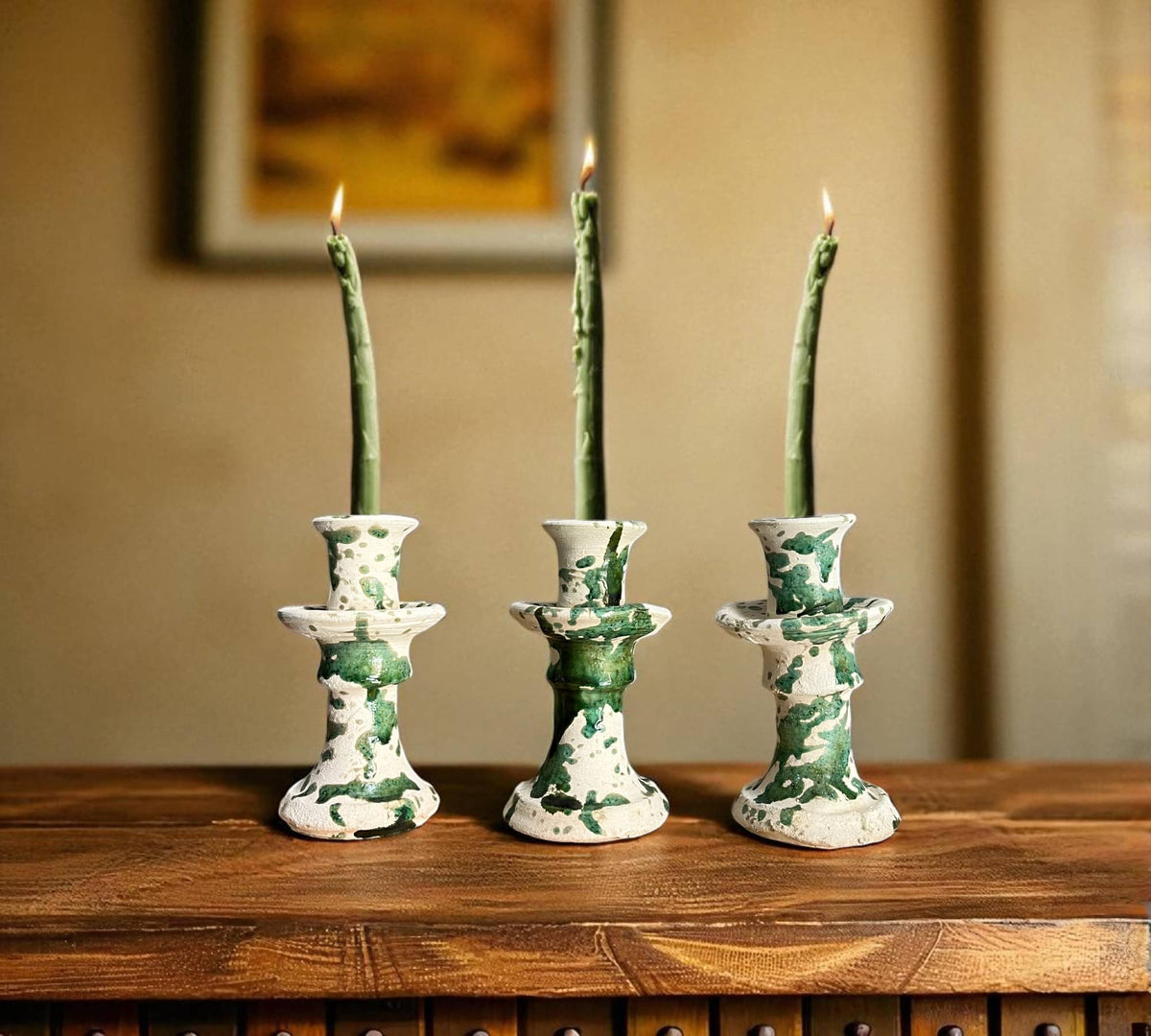 Three green and white ceramic candle holders with lit candles on a wooden surface.