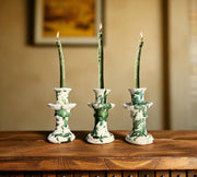 Three green and white ceramic candle holders with lit candles on a wooden surface.