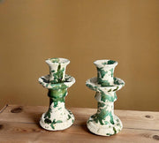 Two green and white ceramic candle holders on a wooden surface with a beige background