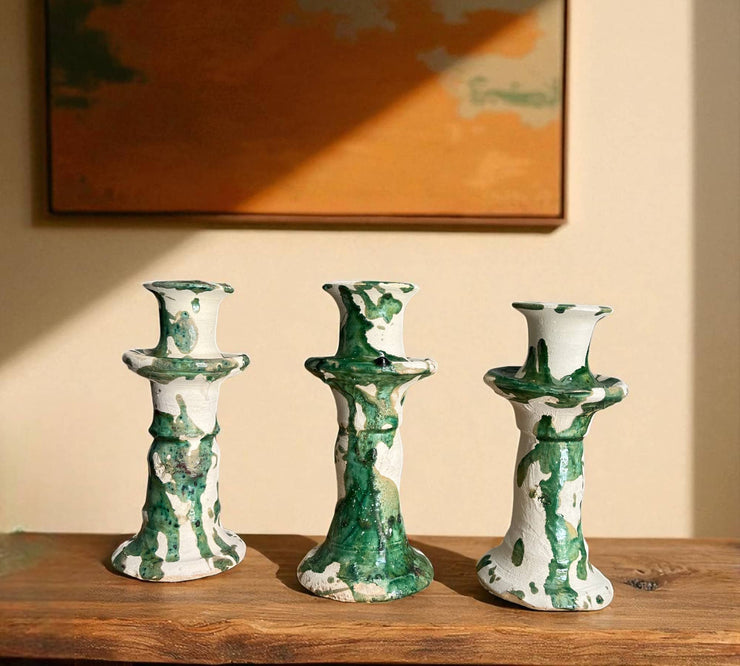 Three green and white ceramic candle holders on a wooden surface with a painting in the background.
