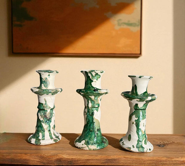 Three green and white ceramic candle holders on a wooden surface with a painting in the background.