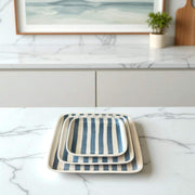 Set of three striped trays on a marble countertop with a framed picture and plant in the background.
