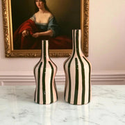 Two striped vases on a marble surface with a painting in the background