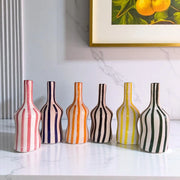 Set of six striped ceramic vases on a marble surface with a framed picture in the background.