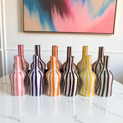 Set of colorful striped vases on a marble surface with abstract art in the background.