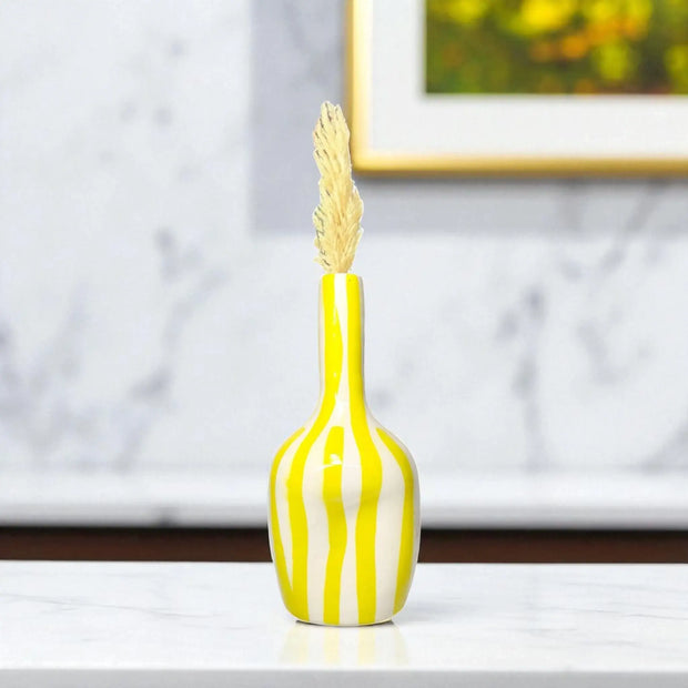 Decorative vase with yellow and white stripes and a wheat sheaf on top, placed on a surface with a blurred background.