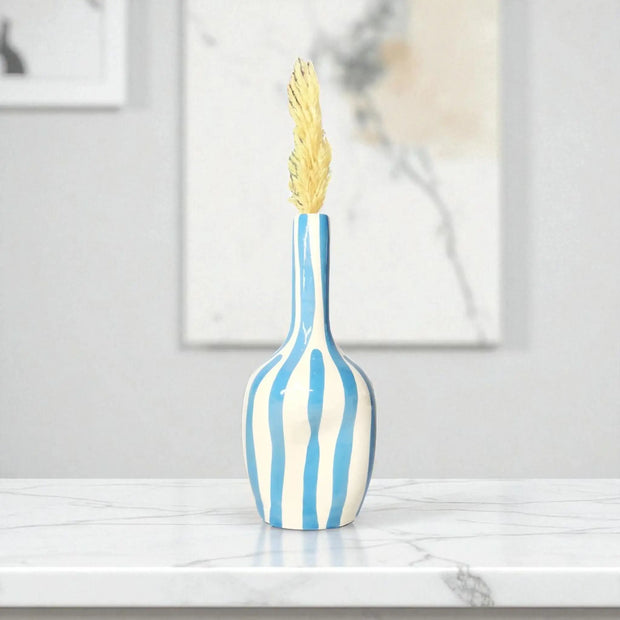 Decorative vase with blue and white stripes and a gold leaf on a marble surface.