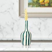 Decorative vase with green and white stripes on a marble surface, framed artwork in the background.