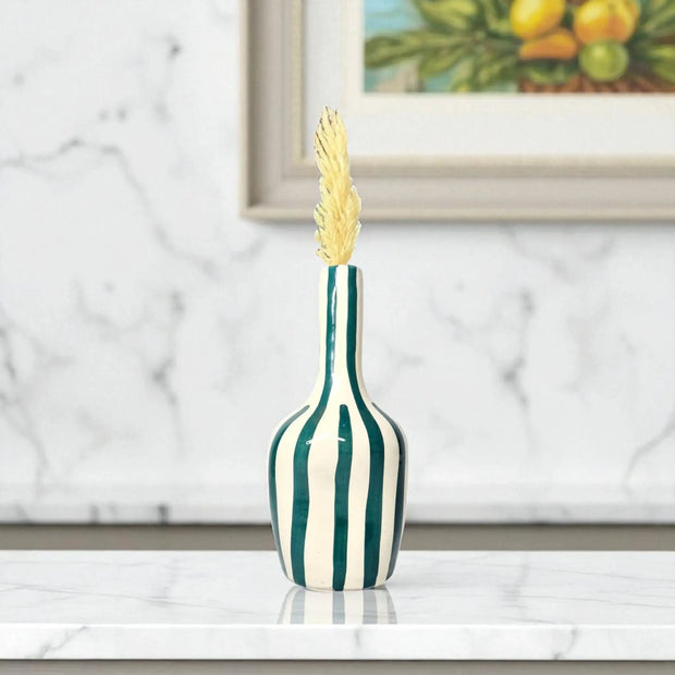 Decorative vase with green and white stripes on a marble surface, framed artwork in the background.