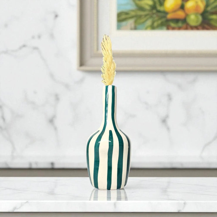 Decorative vase with green and white stripes on a marble surface, framed artwork in the background.