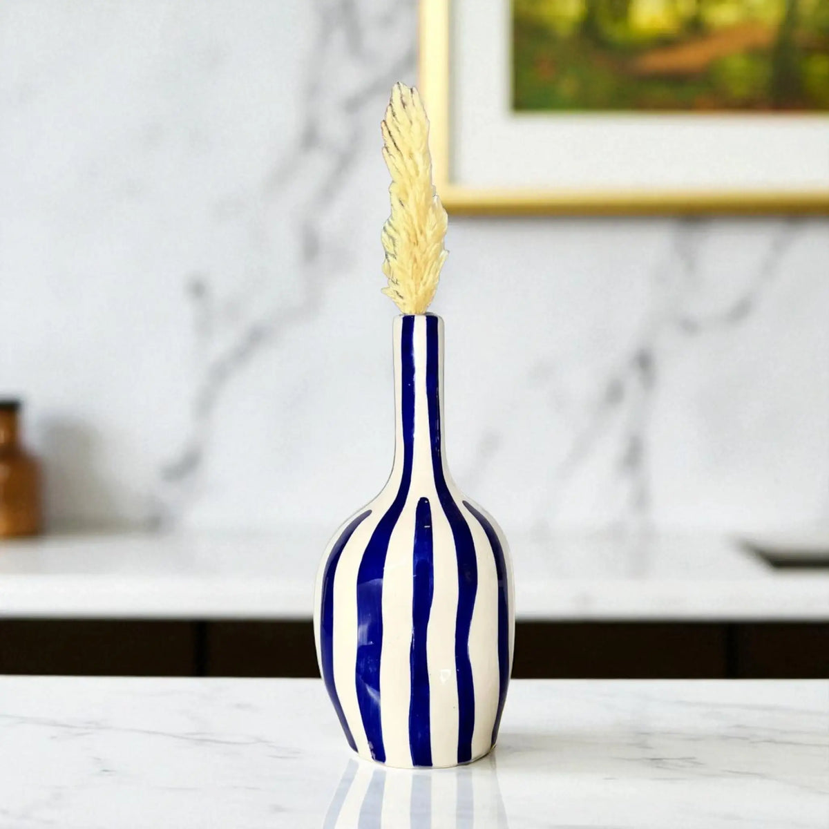 Blue and white striped vase with a gold leaf on a marble surface