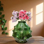 Green textured vase with pink and white flowers on a wooden surface