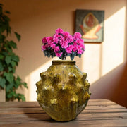 Vintage-style yellow vase with textured surface holding pink flowers on a wooden surface.