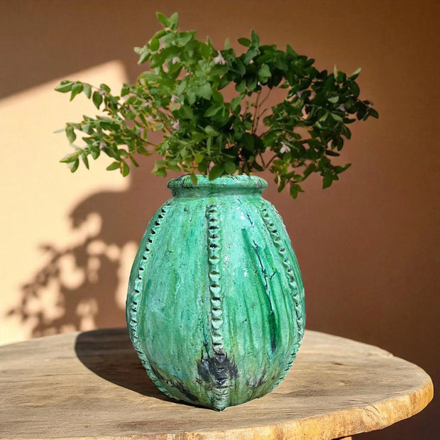 Green textured vase with plants on a wooden surface against a brown background