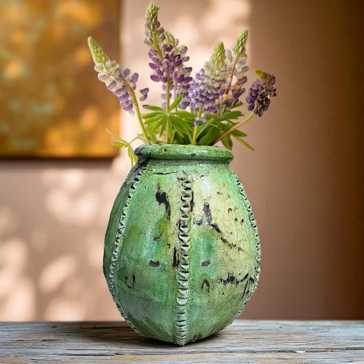 Green textured vase with purple flowers on a wooden surface