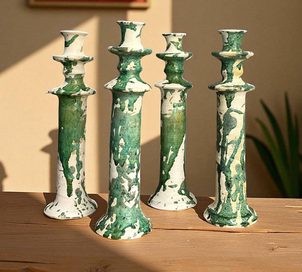 Set of four green and white ceramic candle holders on a wooden surface with a neutral background.