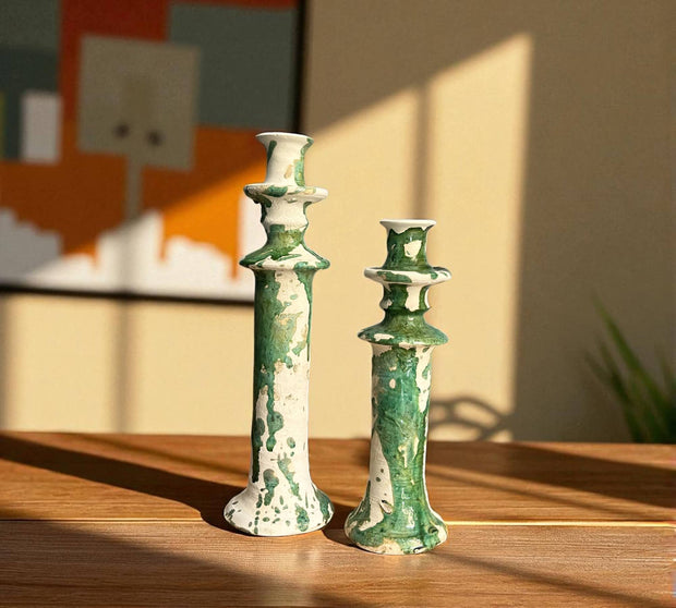 Two green ceramic candle holders on a wooden surface with a blurred background